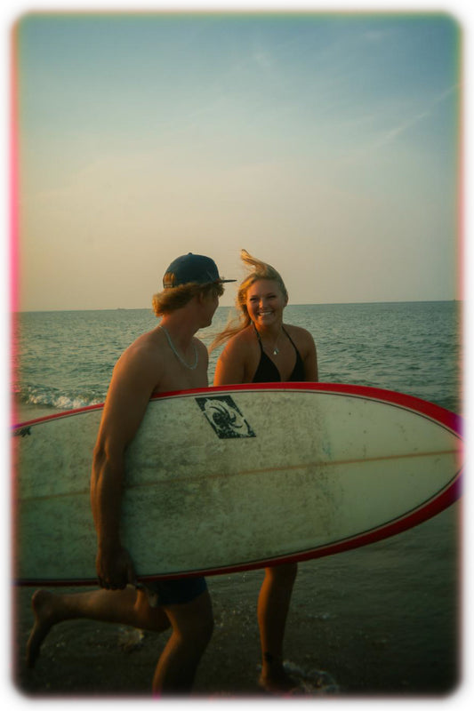Two people with a surfboard on a beach at sunset