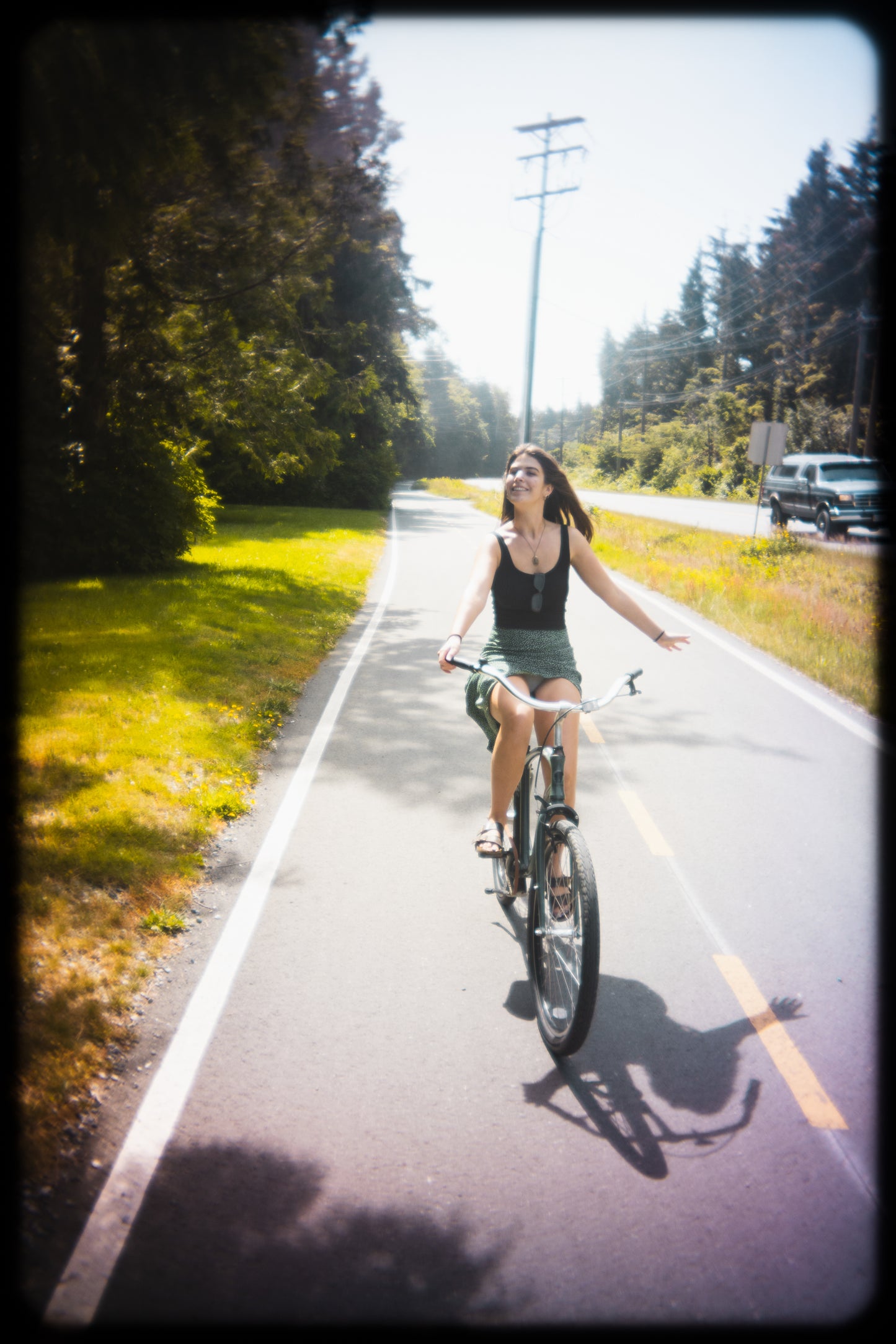 Woman riding a bicycle on a paved path with trees and a clear sky in the background