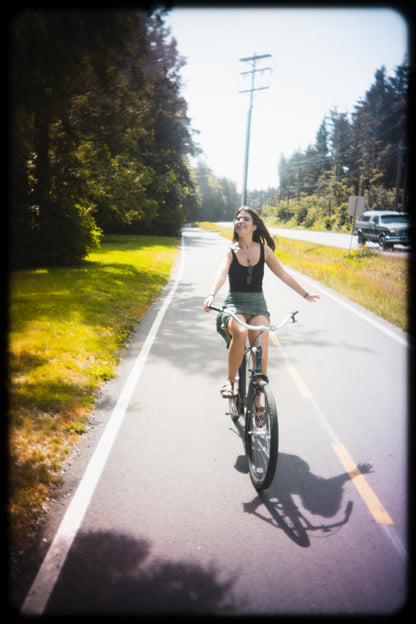 Woman riding a bicycle on a paved path with trees and a clear sky in the background