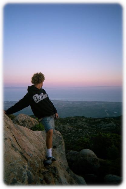 Person standing on a rocky outcrop overlooking a vast landscape at dusk.
